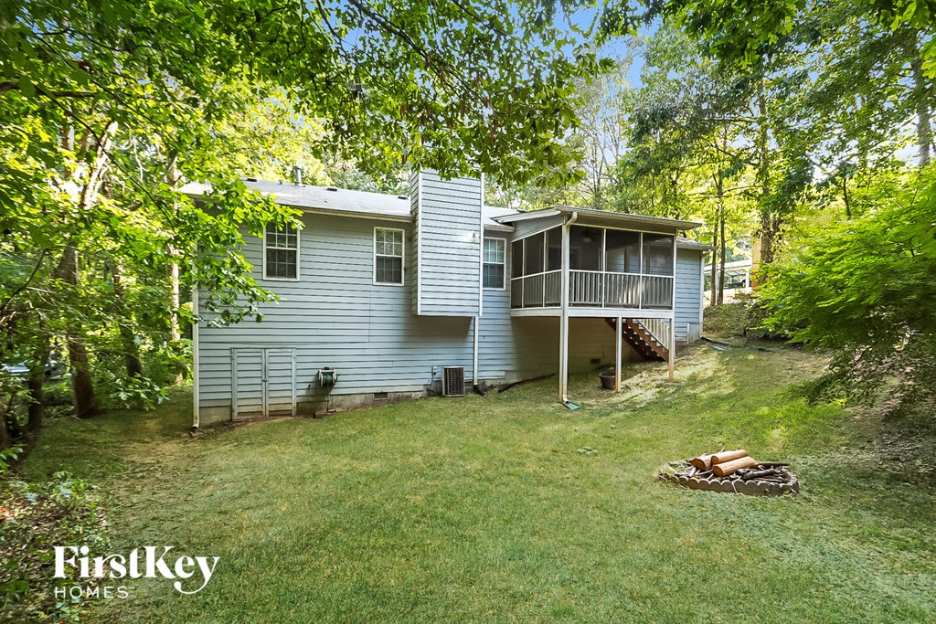 the back of a blue house with a porch and a yard with trees