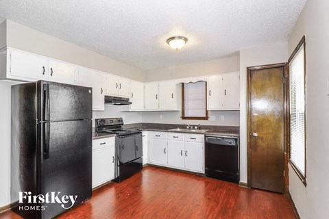 A kitchen with a black fridge and wooden floors.
