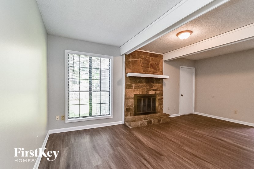 an empty living room with a stone fireplace and wooden floors