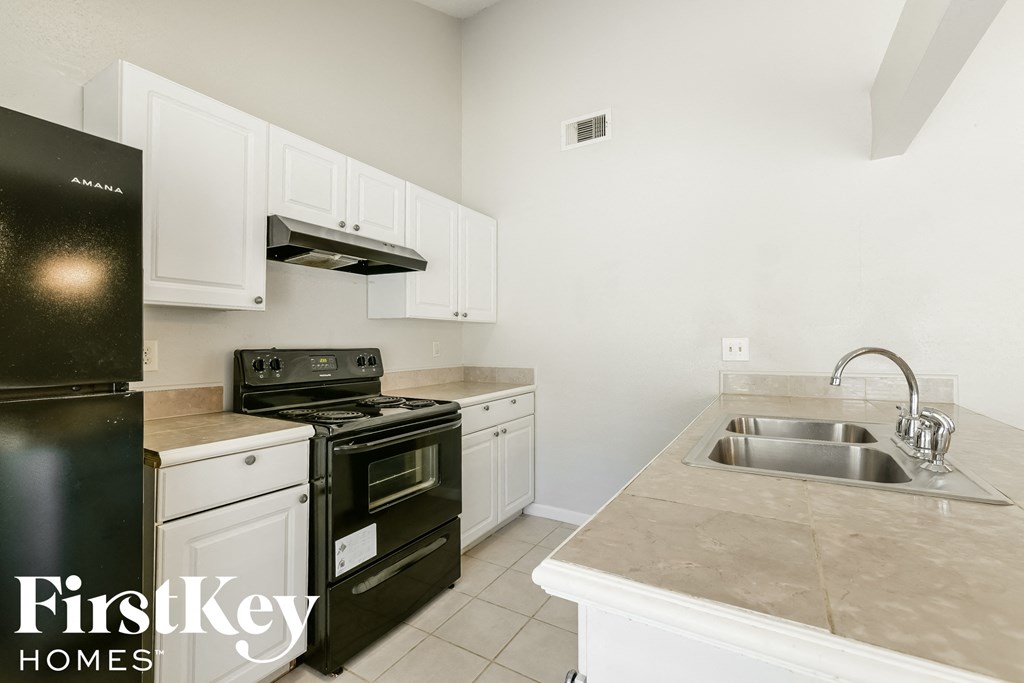 A kitchen with a black fridge and white cabinets.