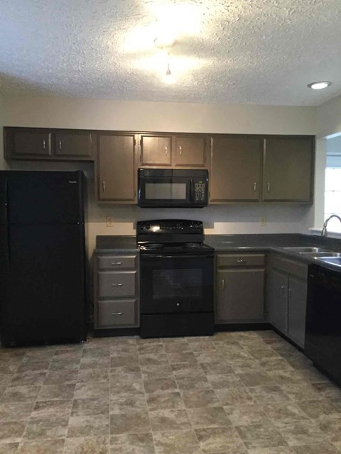 A black refrigerator and oven in a kitchen with brown cabinets.