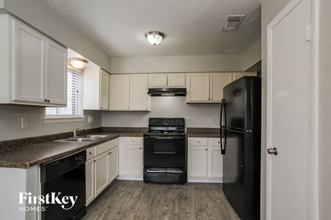 A kitchen with a black refrigerator and white cabinets.