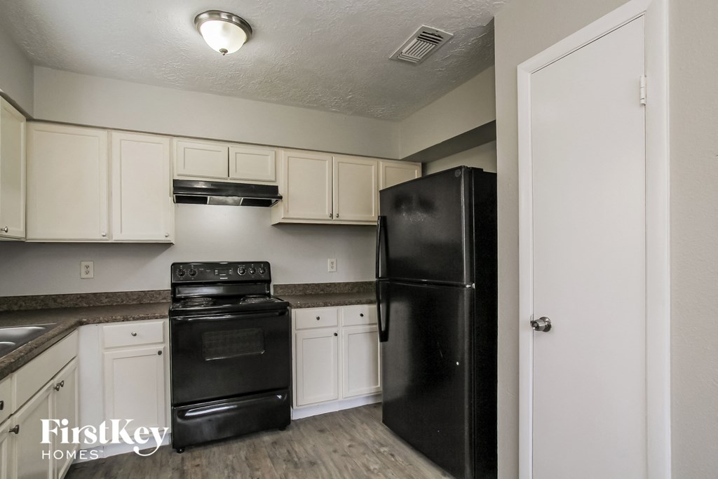 A black refrigerator in a kitchen with white cabinets.