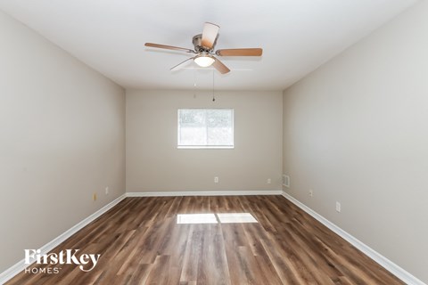 the spacious living room with hardwood flooring and a ceiling fan