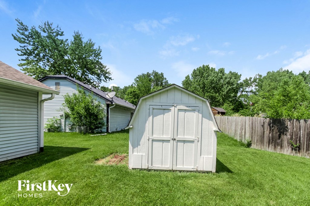 a small white shed in a backyard with a lawn and a fence