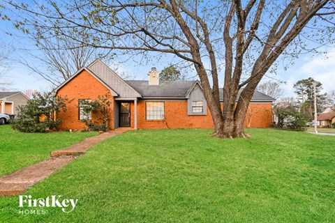 a red brick house with a large tree in the yard
