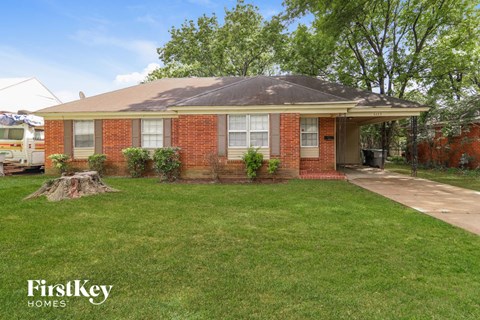 a small brick house with a lawn and a tree stump in the front