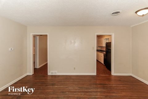 an empty living room with wood flooring and a door to a kitchen