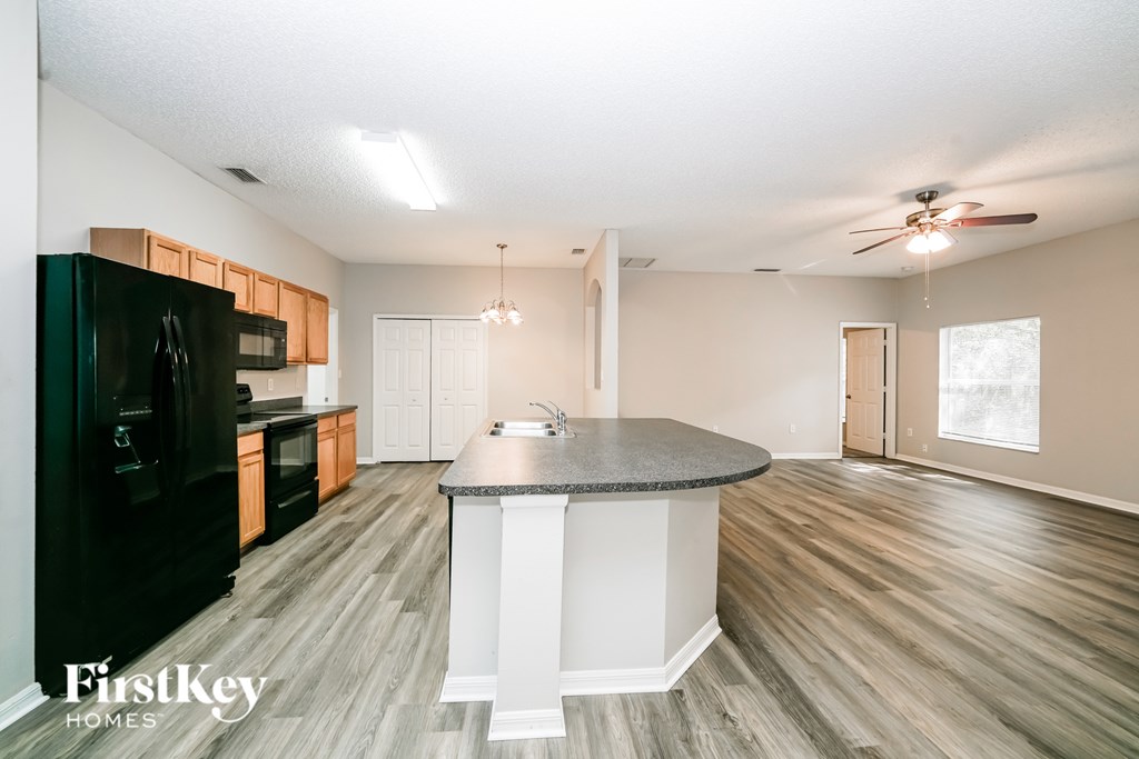 A kitchen with a black fridge and wooden floors.