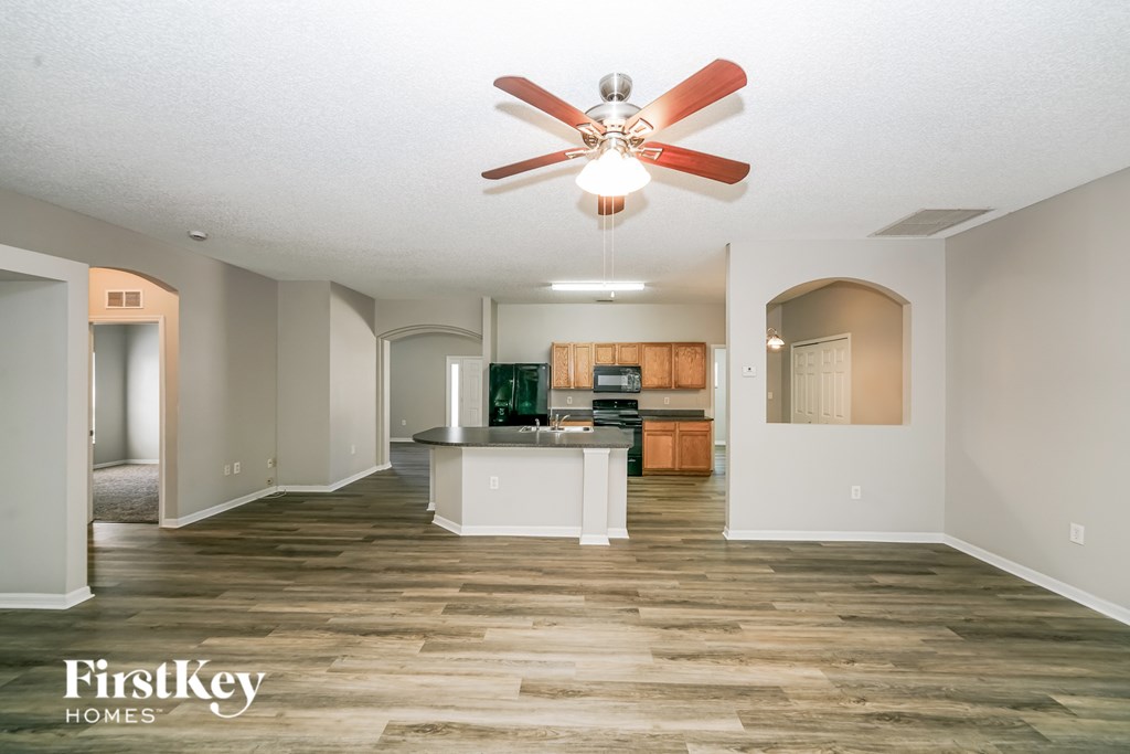 A spacious living room with a kitchen in the background and a fan hanging from the ceiling.