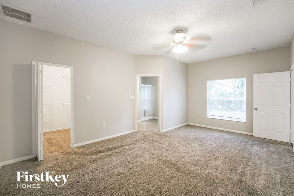A carpeted room with a ceiling fan and three doors.