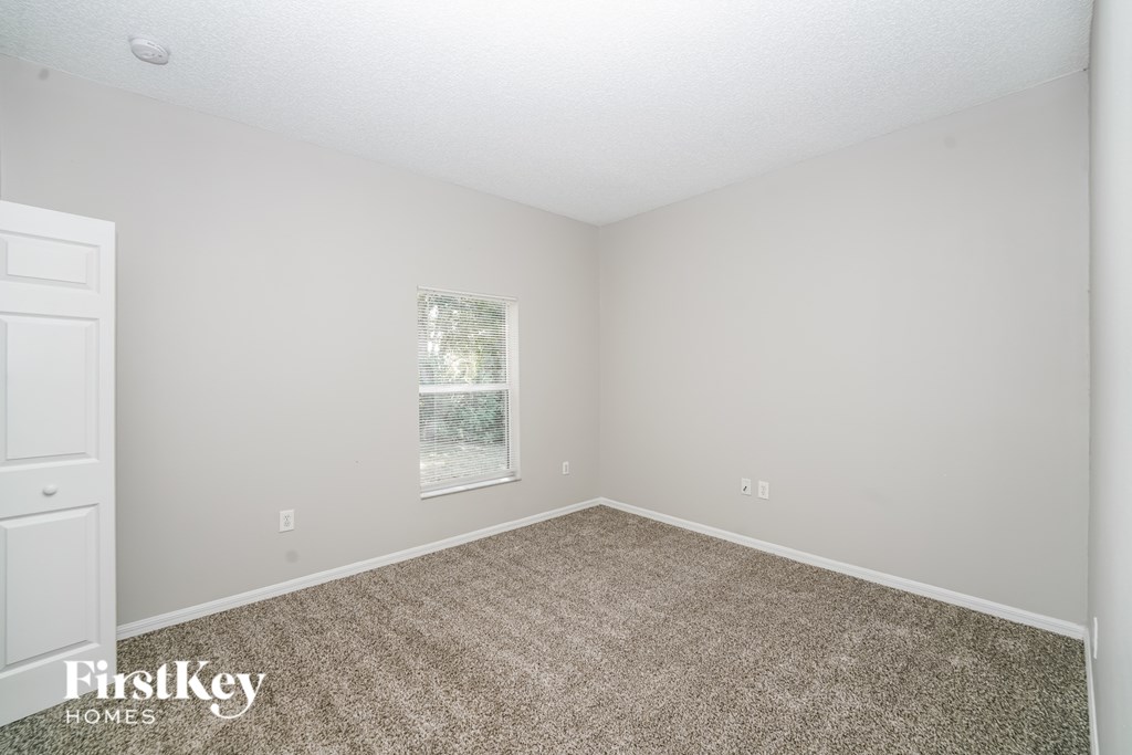 A room with a carpeted floor and a window with a view of trees.