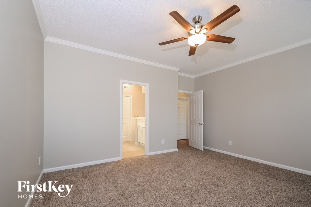 an empty living room with a ceiling fan and a door to a bathroom
