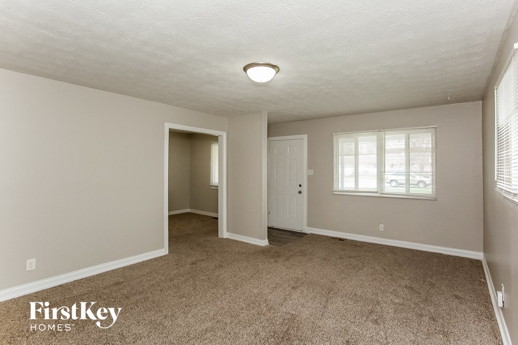 A spacious room with a carpeted floor and a window with blinds.
