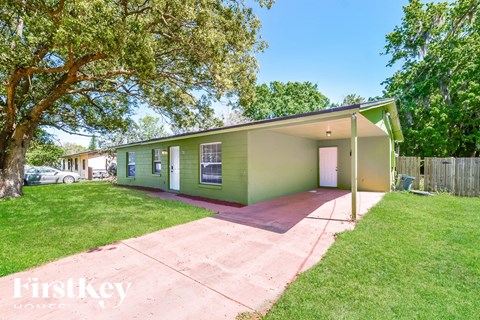 a green house with a driveway and a tree