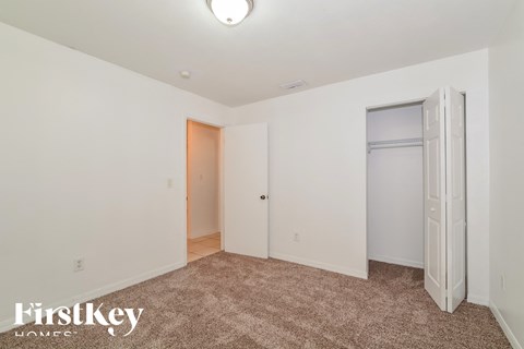 a bedroom with white walls and carpet and a door to a closet