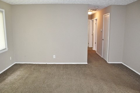 an empty room with a carpeted hallway and a door to a bedroom