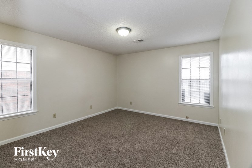 A room with a carpet floor and two windows.