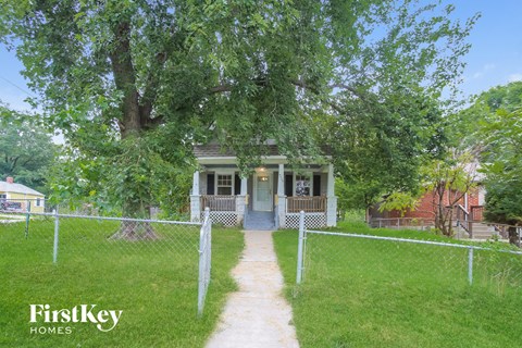 A house with a porch and a fence in front of it.