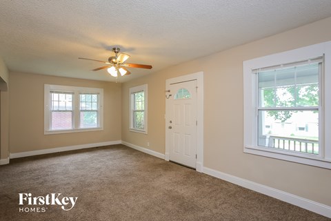 A room with a carpet floor, a ceiling fan, and a door.