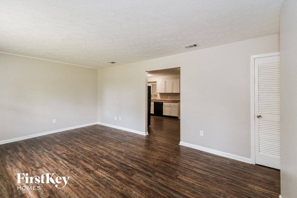 an empty living room with wood flooring and a kitchen