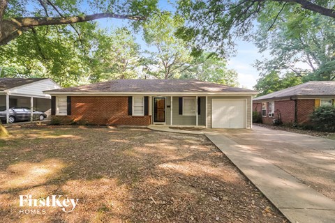 a small brick house with a driveway and a tree