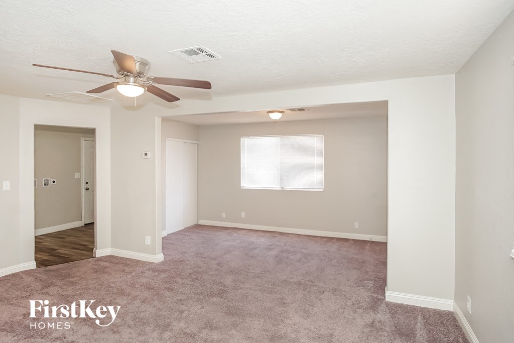 an empty living room with a ceiling fan and a door to a hallway