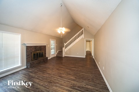 A spacious room with wooden floors and a staircase leading to the upper level.