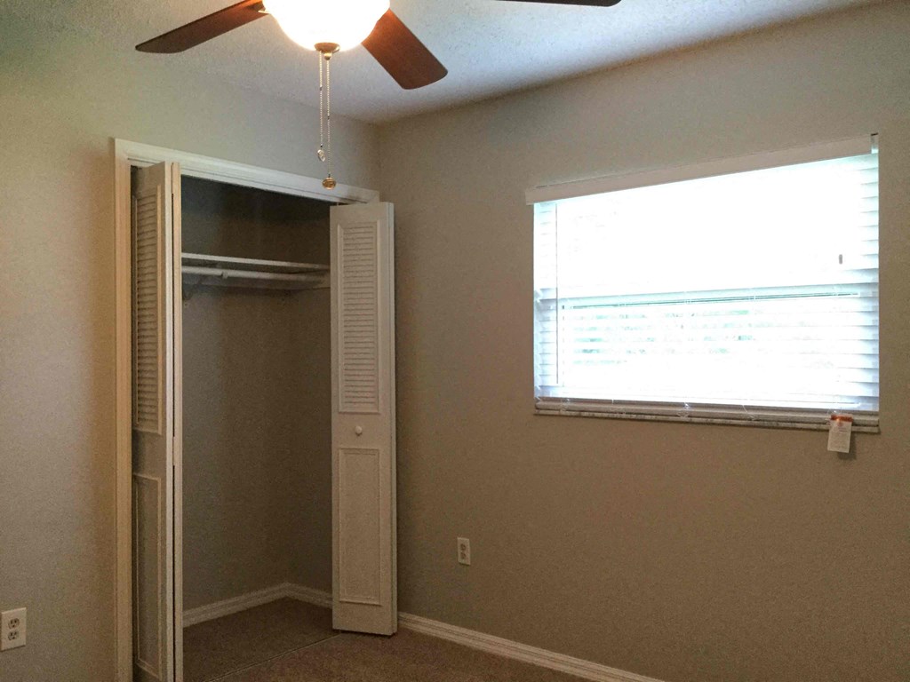 a bedroom with a closet and a window and a ceiling fan