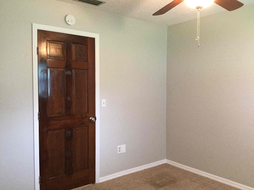 a empty room with a wooden door and a ceiling fan