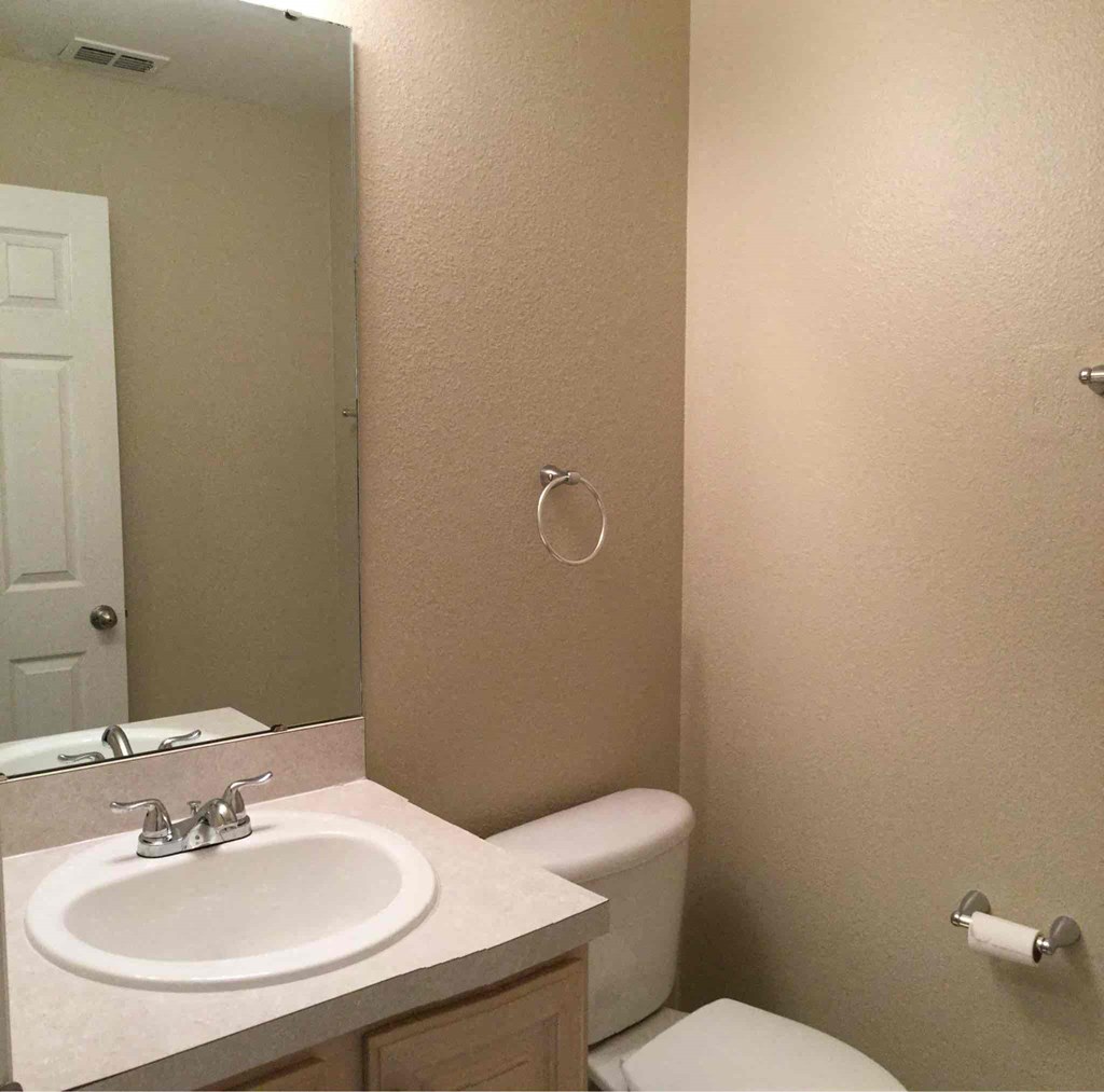 A bathroom with a toilet, sink, and mirror.