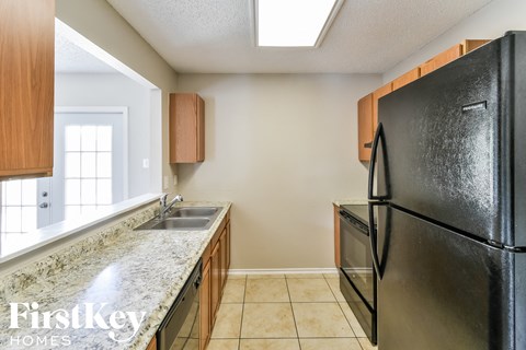 A kitchen with a black refrigerator and a granite countertop.