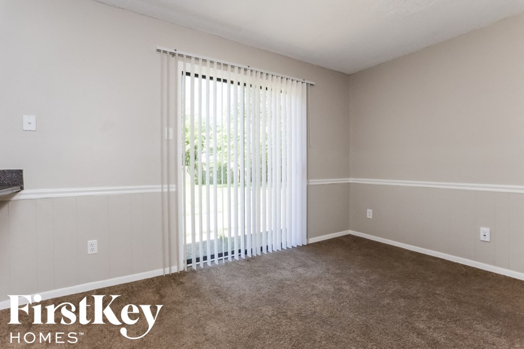 A room with a carpeted floor and a window covered with white blinds.