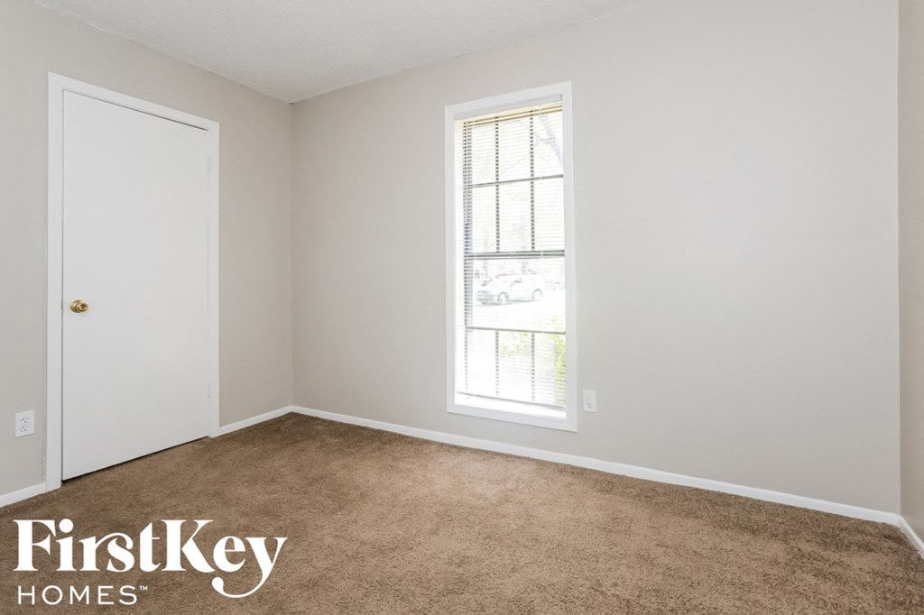 A room with a carpeted floor, a window, and a door.
