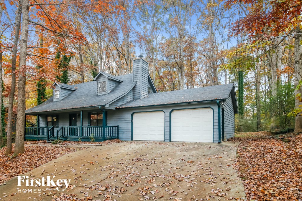 A house with a grey roof and a white garage door is surrounded by trees with orange leaves.
