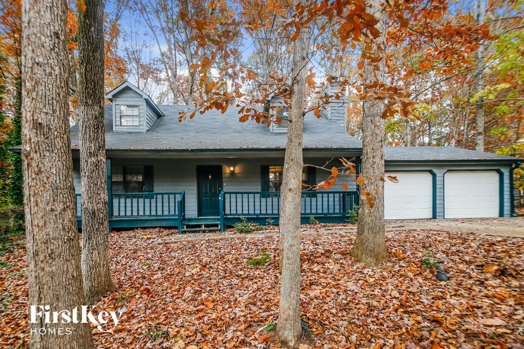 A house with a blue front porch surrounded by trees with orange leaves.