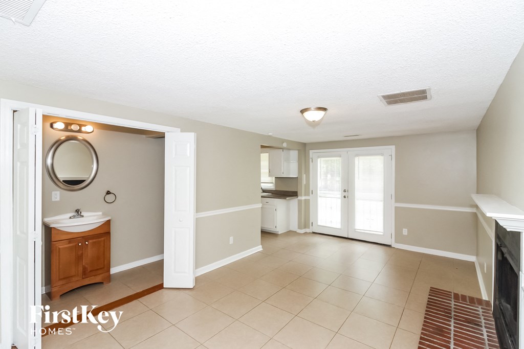 A spacious bathroom with a sink, mirror, and a large open doorway leading to another room.