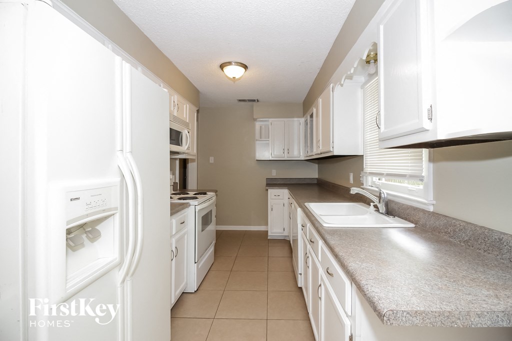 A white kitchen with a refrigerator on the left and a sink on the right.