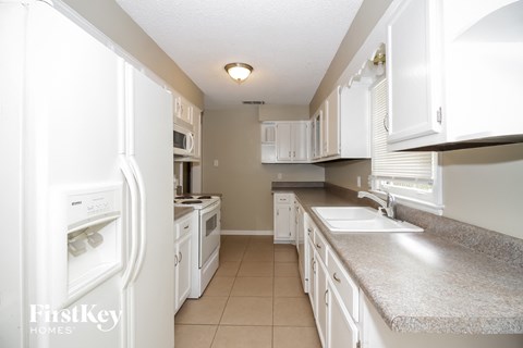 A white kitchen with a refrigerator on the left and a sink on the right.