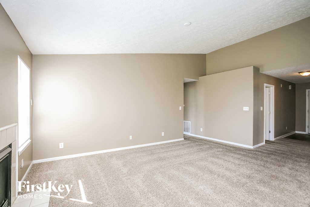 A spacious room with beige carpeting and walls, and a doorway leading to another room.