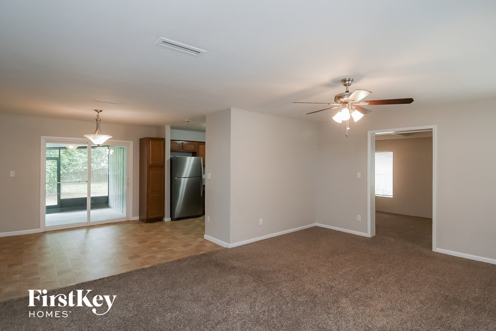 an empty living room with a ceiling fan and a refrigerator