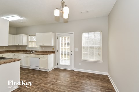 an empty kitchen with white cabinets and a door to the living room
