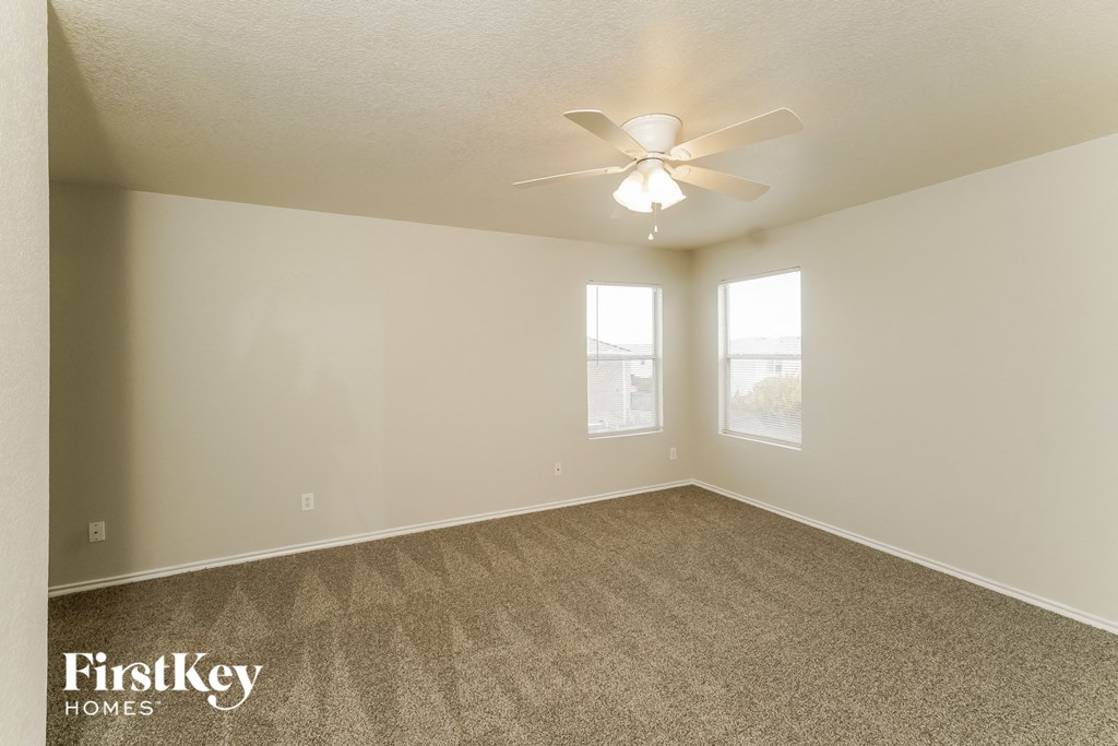 an empty living room with a ceiling fan and two windows
