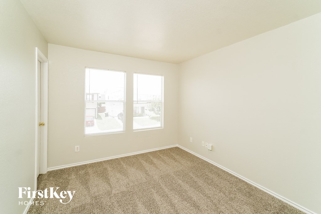 a spacious living room with carpet and two windows