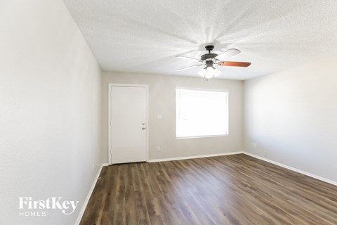 the spacious living room with hardwood flooring and a ceiling fan