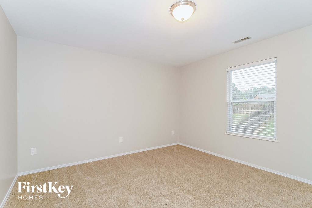 a spacious bedroom with a large window and beige carpet