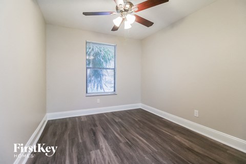 A room with a ceiling fan and a window with a view of trees.