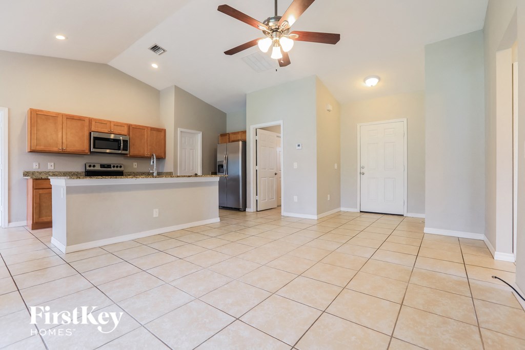 A spacious kitchen and living room with a ceiling fan and tiled flooring.