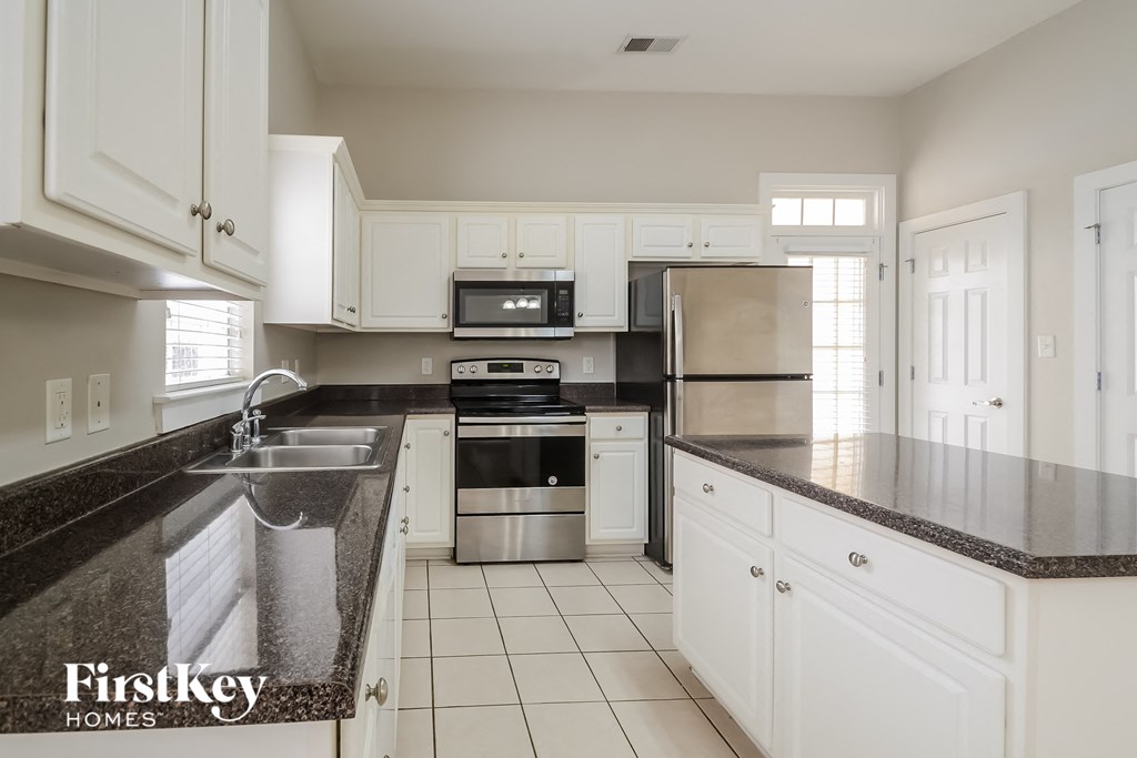A kitchen with white cabinets and a black counter top.