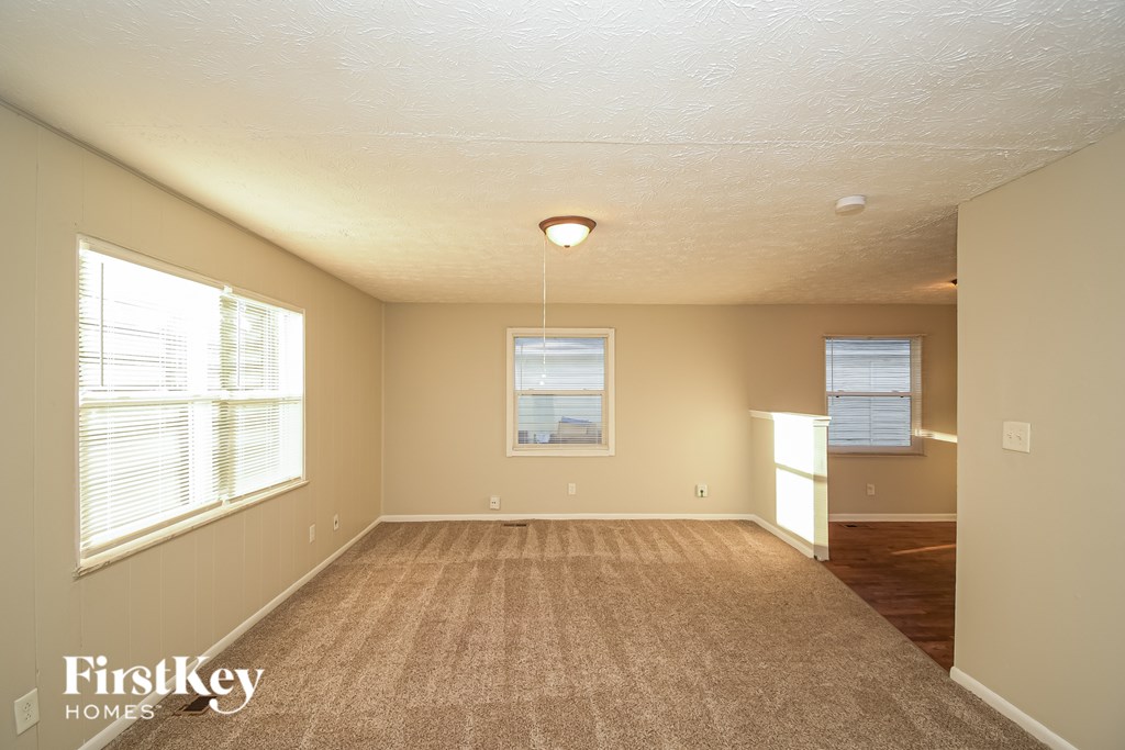 A spacious room with a carpeted floor and two windows.
